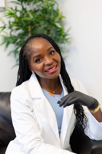 Dr Lian Peter wearing a white lab coat and black surgical gloves with a syringe in her hand